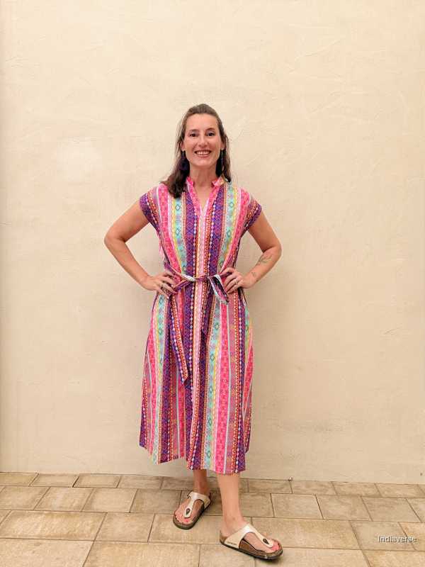 Woman wearing a colorful striped dress standing against a beige wall.