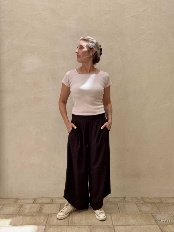 Woman is standing in front of beige wall wearing black long pants