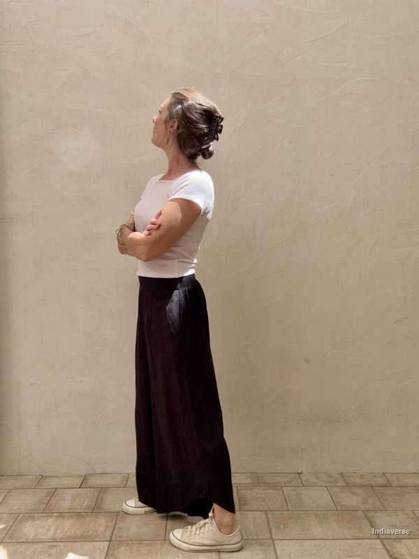 Woman standing with arms cross in front of beige wall wearing black loose pants
