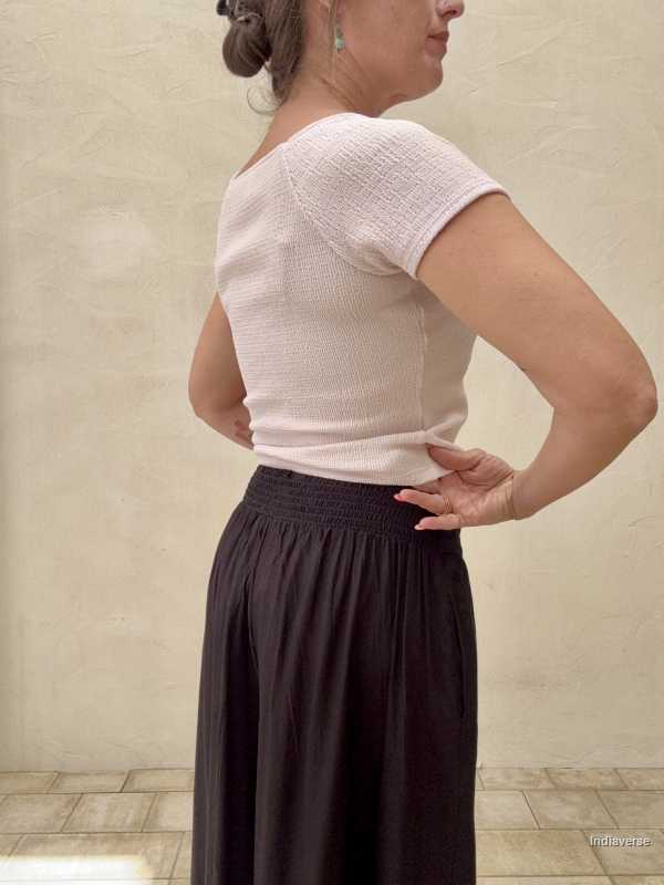 View from behind of black pants showing the pleated fabric against a beige wall