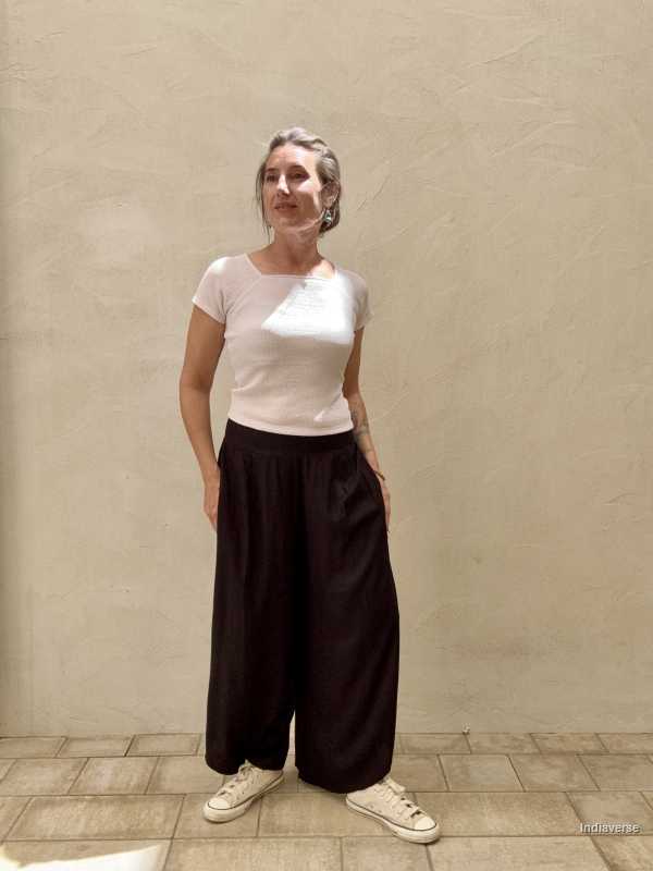 Woman standing casually in front of beige wall wearing black pants and white top