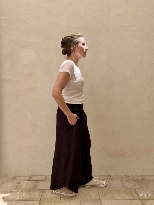 side view of woman and beige background wearing wide black pants and white top