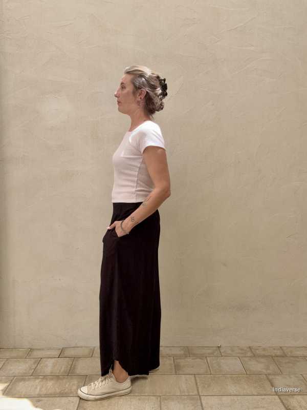 Side view of woman with hands in the pockets of her black pants in front of beige wall