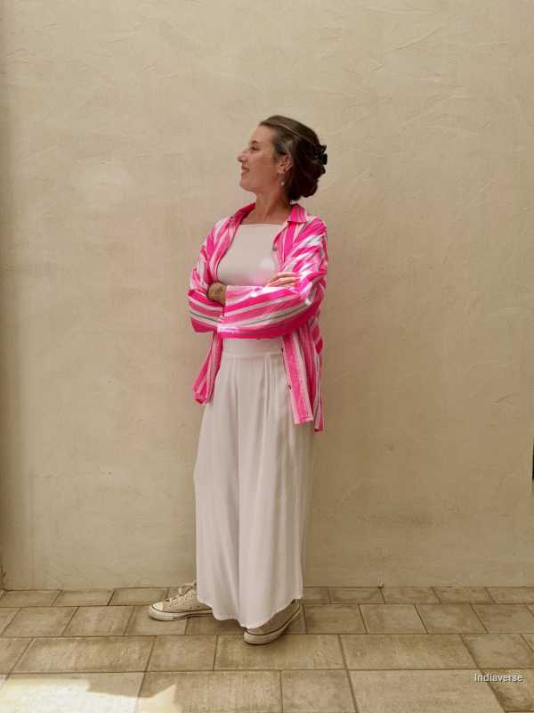 Woman wearing a pink and white striped cardigan over a white top and light-colored pants, standing against a beige wall.