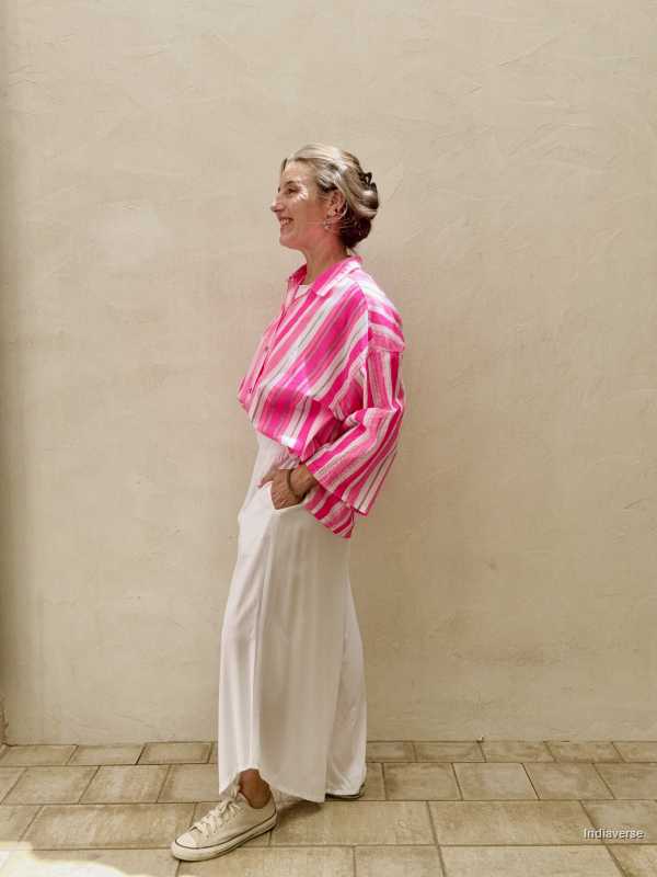 Person wearing a bright pink and white striped shirt with white pants against a beige wall.
