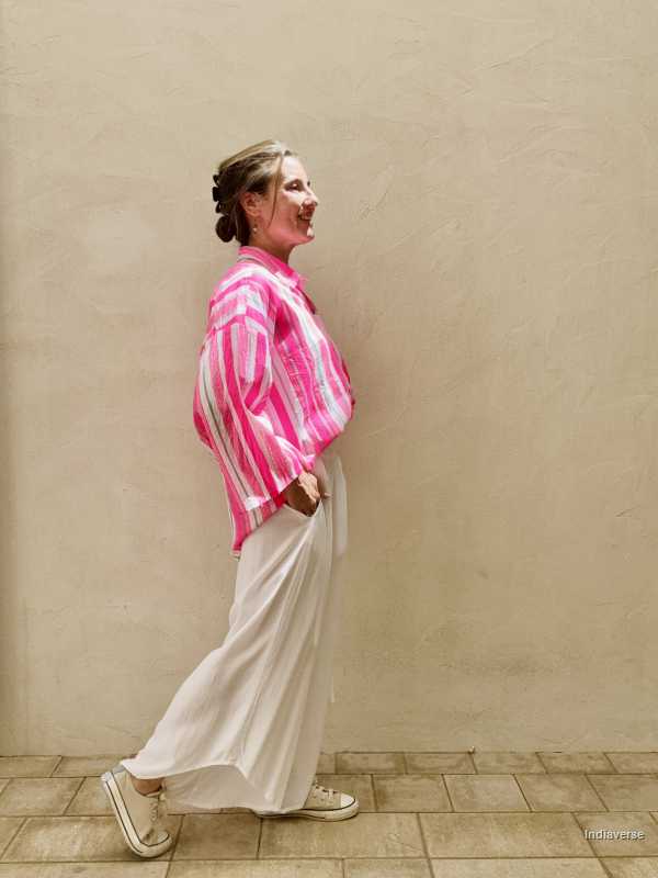Person wearing a pink and white striped shirt and white pants against a beige wall.