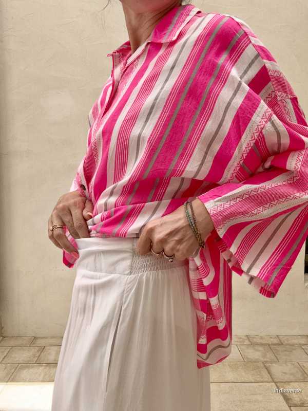 Person wearing a pink and white striped shirt with a patterned shawl over shoulders against a neutral background.