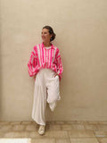 Person wearing a pink and white striped shirt with white pants against a beige wall.