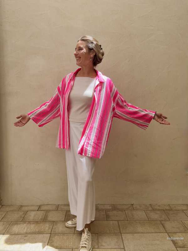 Woman wearing a pink and white striped jacket over a white outfit against a beige wall.