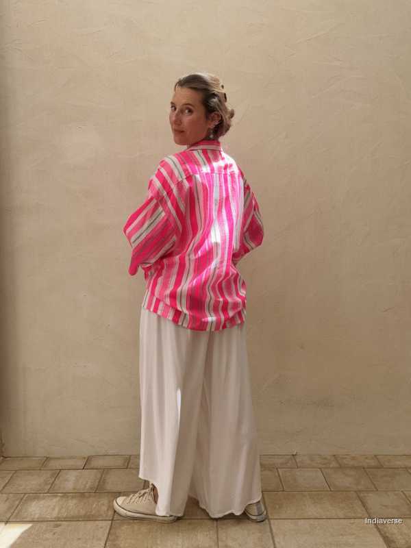 Person wearing a pink and white striped shirt with white pants against a beige wall.