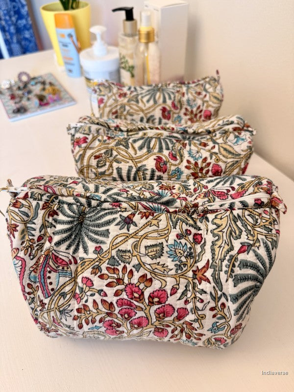 Three fabric cosmetic pouches with a vintage botanical block print pattern in pink, green, and gold on an off-white background, arranged on a light-colored tabletop | Palm Paradise