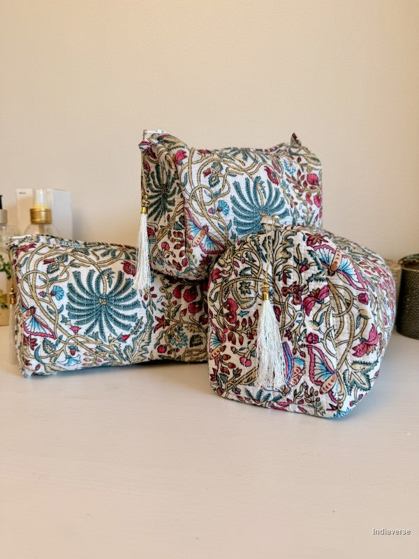 Three decorative floor poufs with a colorful floral and paisley block print on a cream base, featuring white tassels, arranged on a light beige surface against a neutral beige wall | Palm Paradise