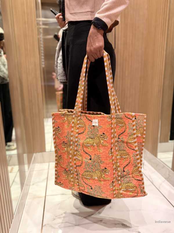 Person holding a colorful tote bag with intricate patterns in an indoor setting.