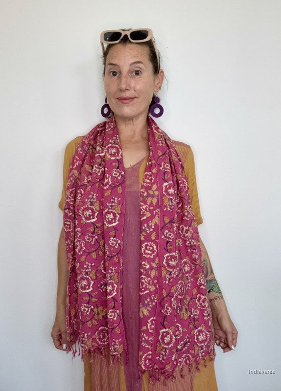 a woman wearing a pink cotton scarf standing in front of a white wall