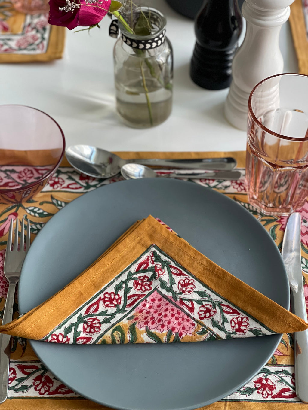 Dining table setting with a gray plate, floral-patterned napkin, and cutlery on a decorative tablecloth.