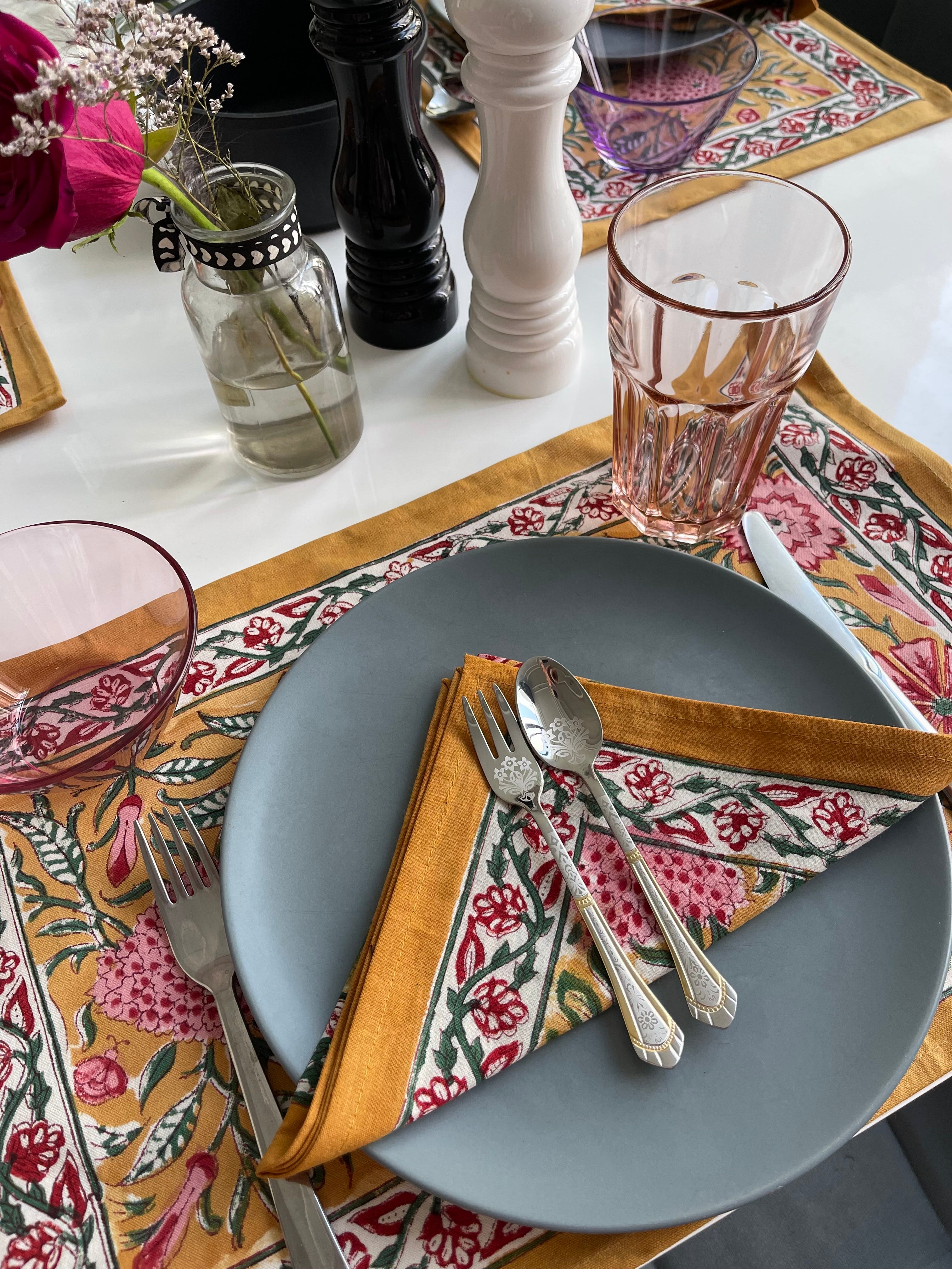 Dining table setting with gray plate, floral napkin, and cutlery on a patterned tablecloth.