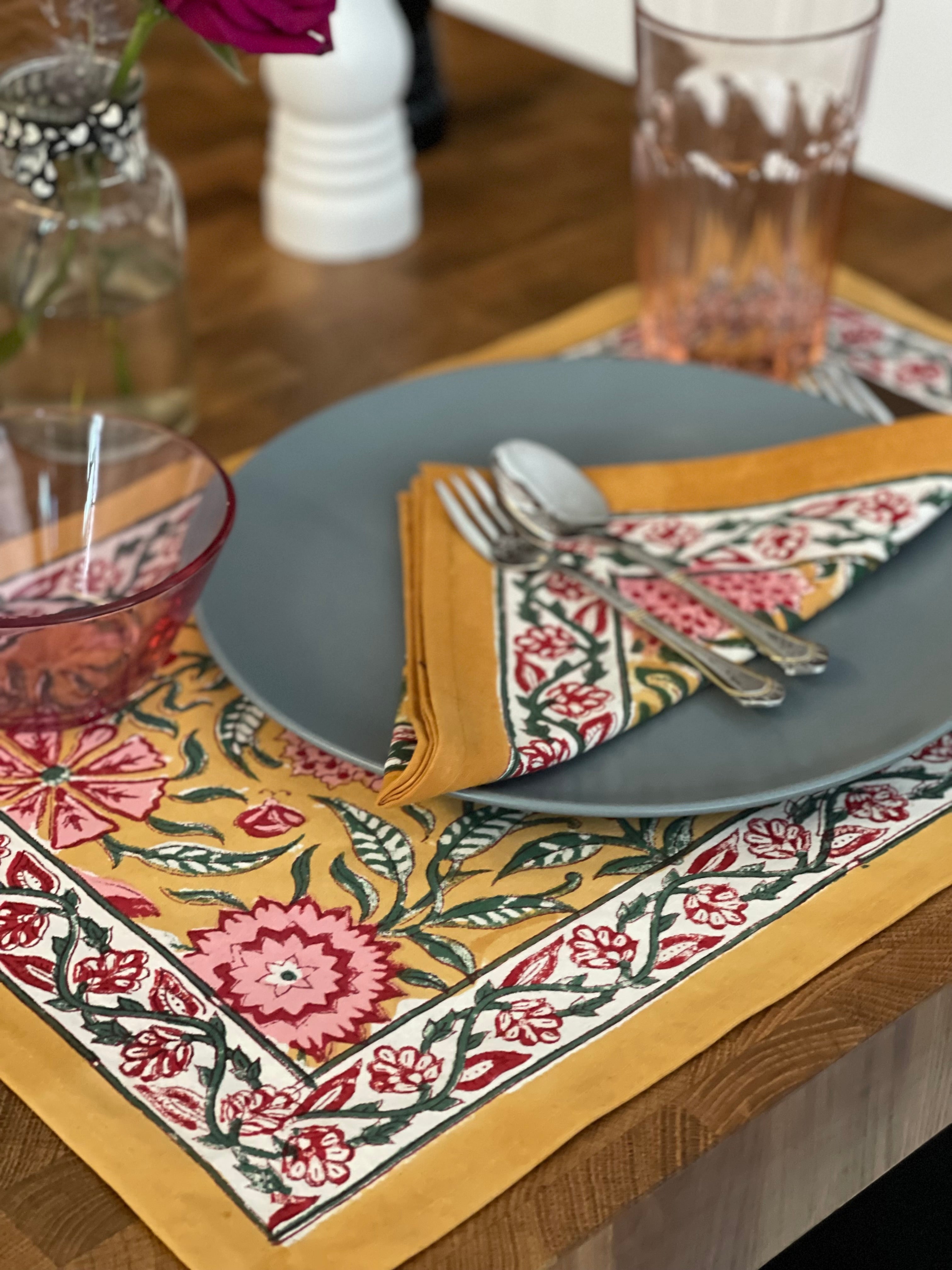 Decorative table setting with floral placemat, gray plate, and cutlery on a wooden table.