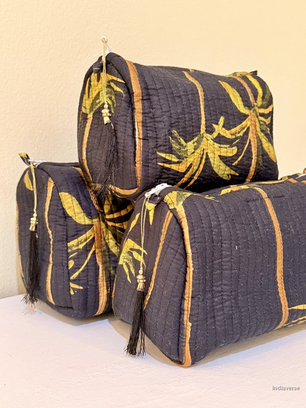 Set of three black toiletry bags with palm tree motif and black tassels stacked together