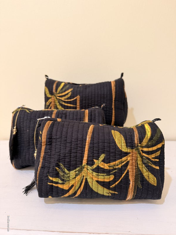 Black Toiletry bags with palm tree design in a set of three together arranged in front of a beige background