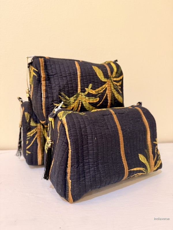 Black Toiletry bags with palm tree design in a set of three together arranged in front of a beige background