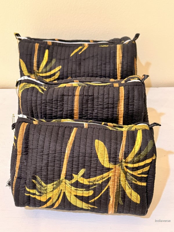 Black Toiletry bags with palm tree design in a set of three together arranged in front of a beige background