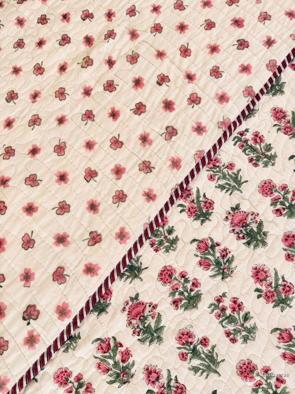 Close up of the front and reverse side of a floral quilted bedspread featuring a pink and green floral pattern on a white background with a decorative red and green border.