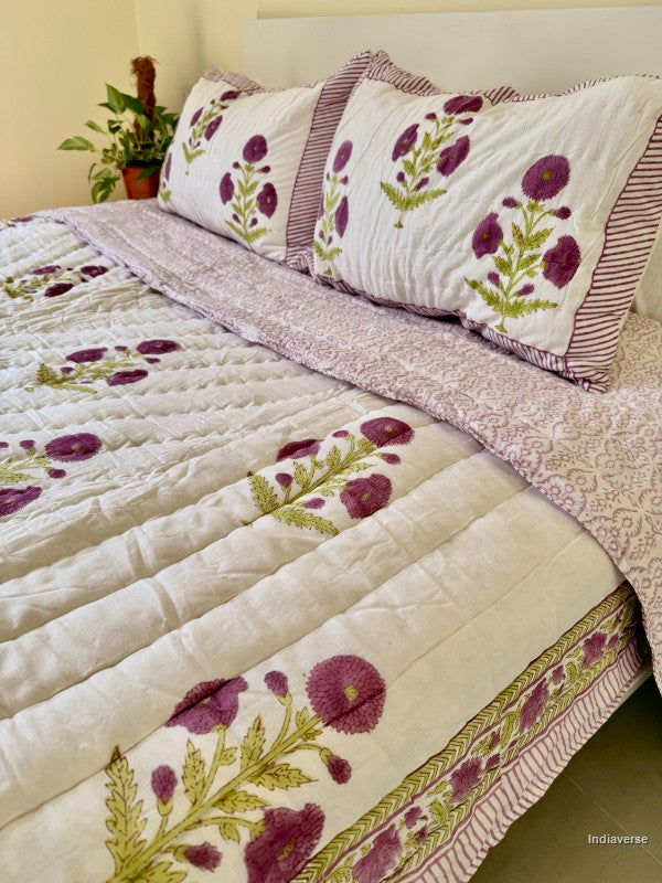 Large white quilted blanket with purple flowers arranged on a white bed in a bedroom with two matching pillowcases