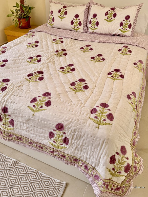 Large white quilted blanket with purple flowers arranged on a white bed in a bedroom with two matching pillowcases
