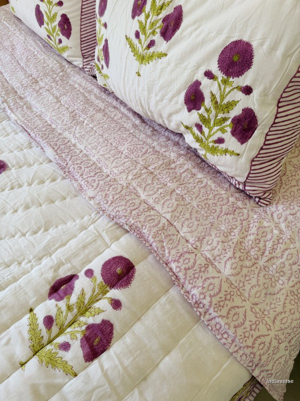 Large white quilted blanket with purple flowers arranged with the purple floral reverse side showing and with two matching pillowcases