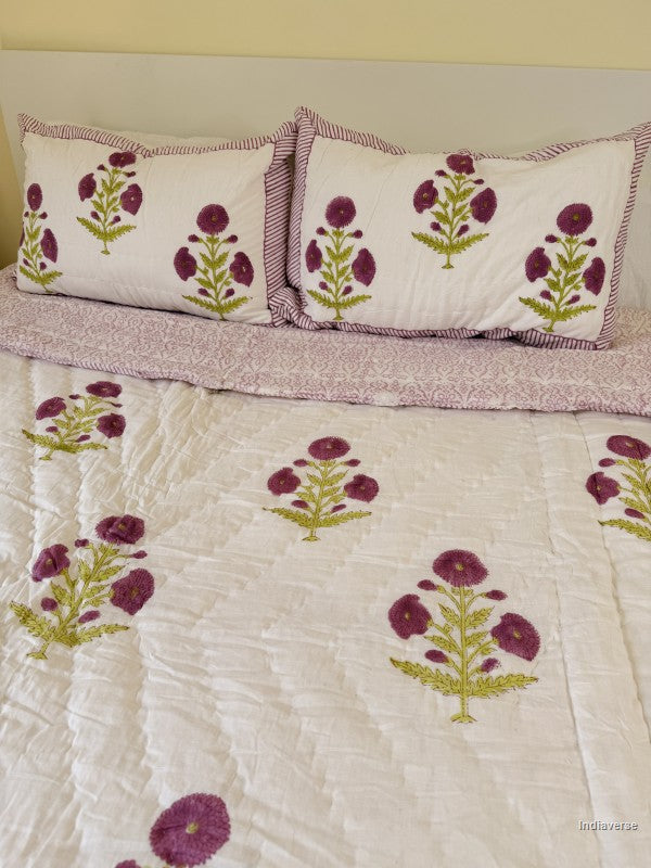 Large white quilted blanket with purple flowers arranged on a white bed in a bedroom with two matching pillowcases