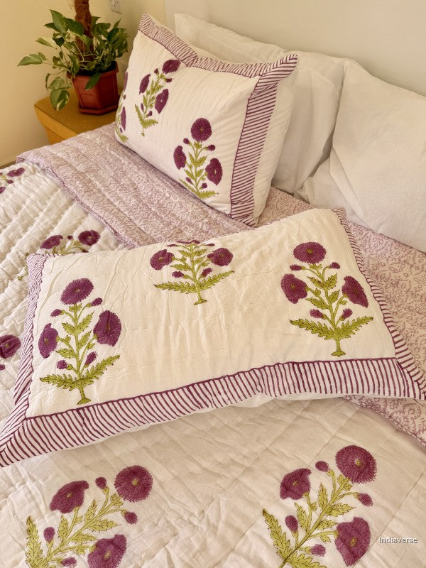 Large white quilted blanket with purple flowers arranged on a white bed in a bedroom with two matching pillowcases