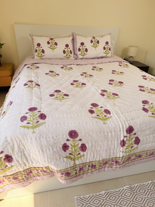 Large white quilted blanket with purple flowers arranged on a white bed in a bedroom with two matching pillowcases
