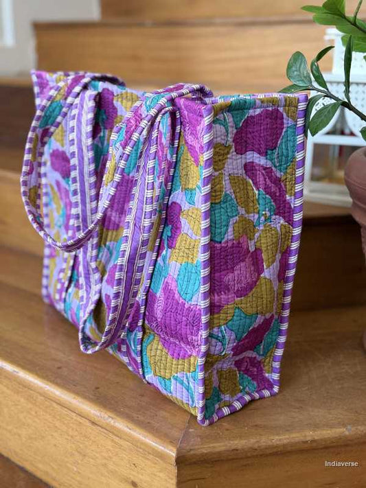 hand block printed quilted cotton tote bag with abstract purple flower design and perfect for shopping and carrying essentials sitting on wooden staircase