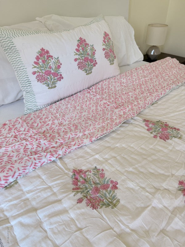 Pink and white floral quilt spread out on a white double bed with a matching pillowcase in a styled bedroom