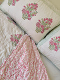 A pink and white floral single quilt spread out and arranged on a white double bed with two matching pillowcases