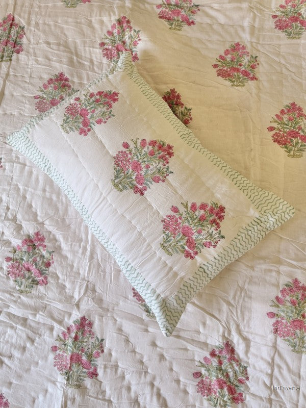 Close up of a pink and white floral pillow case on a matching quilt