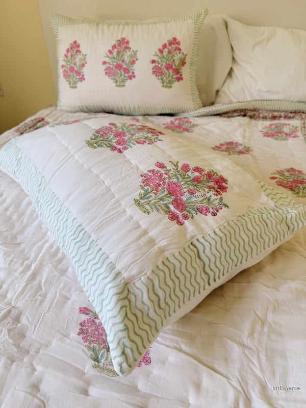 Close up of two pillow cases with pink and white floral quilt spread out on a white double bed
