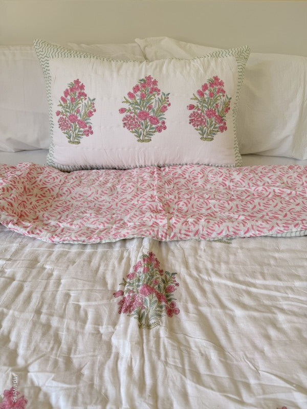 Close up of a pink and white floral quilt spread out on a white double bed with a matching pillowcase