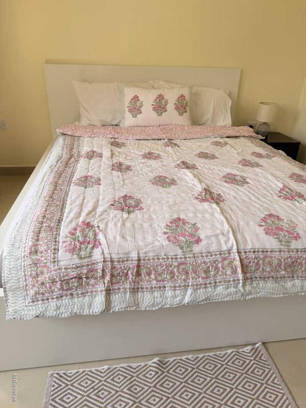 Pink and white floral quilt spread out on a white double bed with a matching pillowcase in a styled bedroom