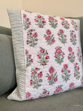 A square quilted throw pillow with a pink and green floral pattern on a white background, featuring a striped green and white border, resting on a gray sofa.