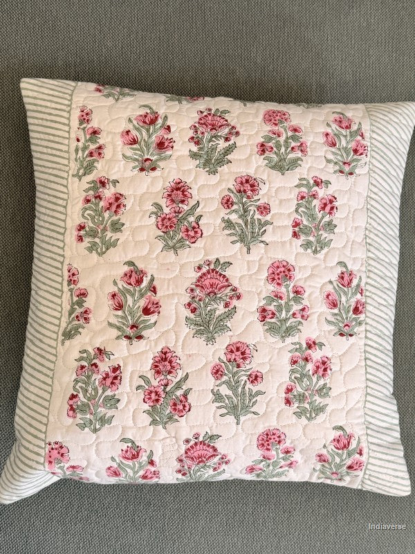 A square quilted throw pillow featuring a pink and green floral pattern on a cream background, with a striped border, shown on a gray textured fabric surface.