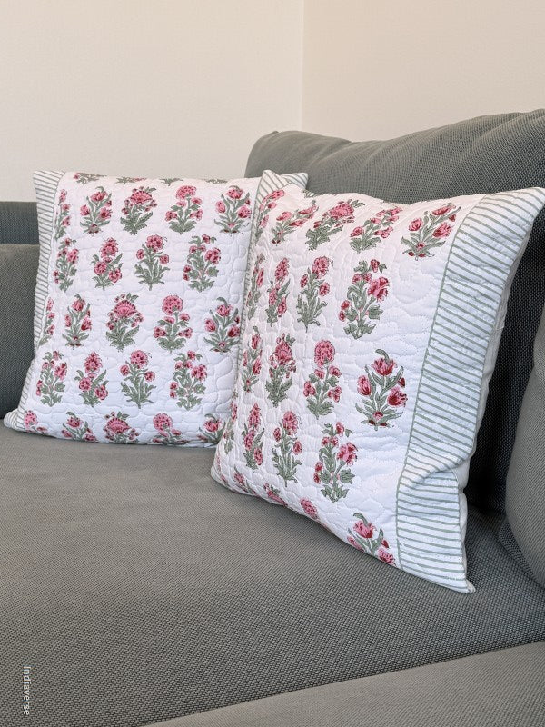 Two decorative throw pillows with a pink and green floral pattern on a white background, featuring striped borders, displayed on a gray fabric sofa.