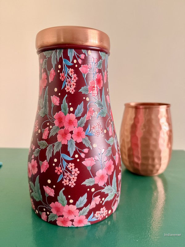decorative water jar with red and pink floral design sitting on a green surface