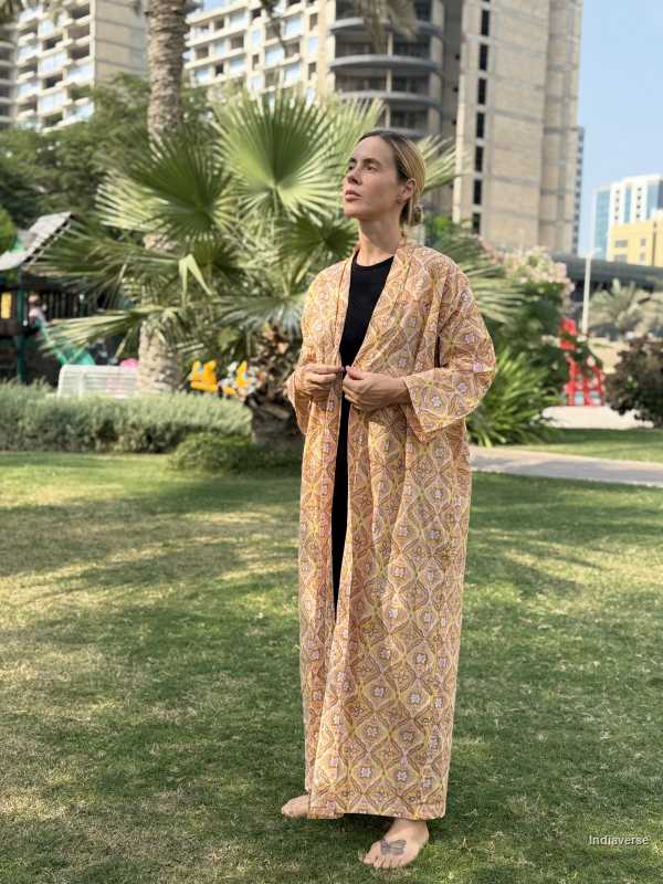 Person wearing a long, patterned robe standing in a park with buildings and palm trees in the background.