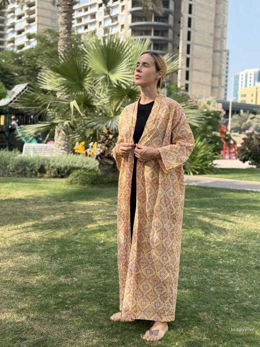 Person wearing a long, patterned robe standing in a park with buildings and palm trees in the background.