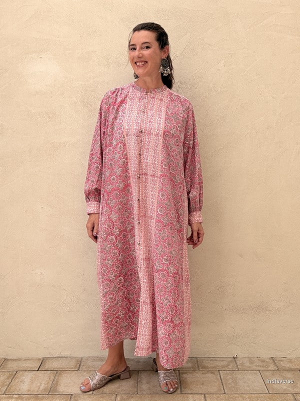 A woman modeling a pink and white patterned long-sleeve tunic dress against a textured beige stucco wall.