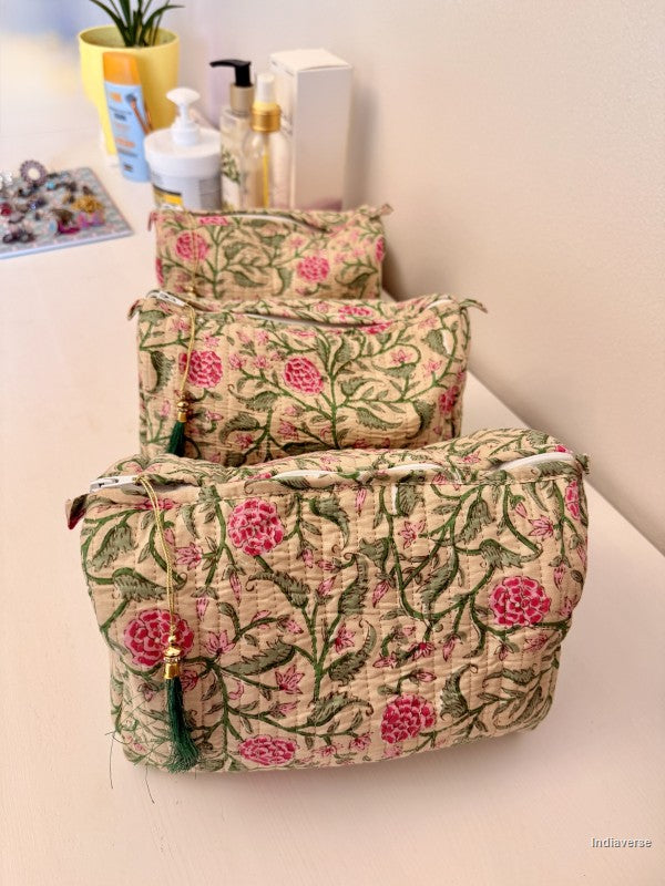 Three quilted fabric cosmetic pouches with a pink and green floral print, arranged on a light-colored vanity surface with toiletries in the background | Rose Garden Beige