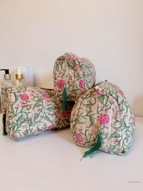 Three quilted fabric cosmetic pouches with a pink and green floral block print on a cream background, arranged on a white surface against a plain off-white wall | Rose Garden Beige