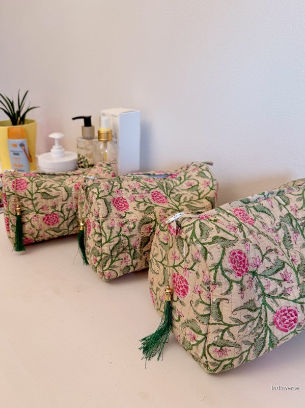 Three rectangular fabric cosmetic pouches with a pink and green floral block print on a beige background, arranged on a light surface with toiletry bottles in the background | Rose Garden Beige