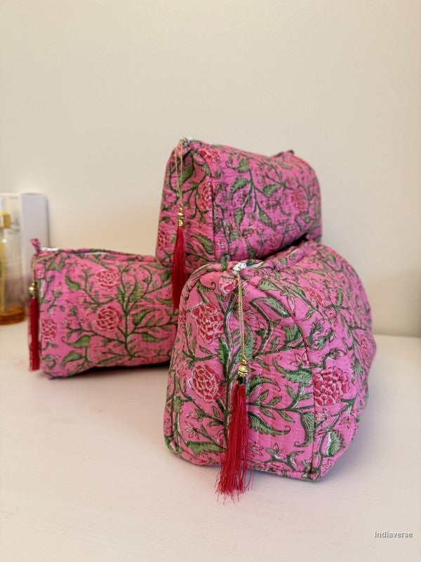 Three pink floral zippered pouches with red tassels, arranged on a white surface against a plain beige wall | Rose Garden